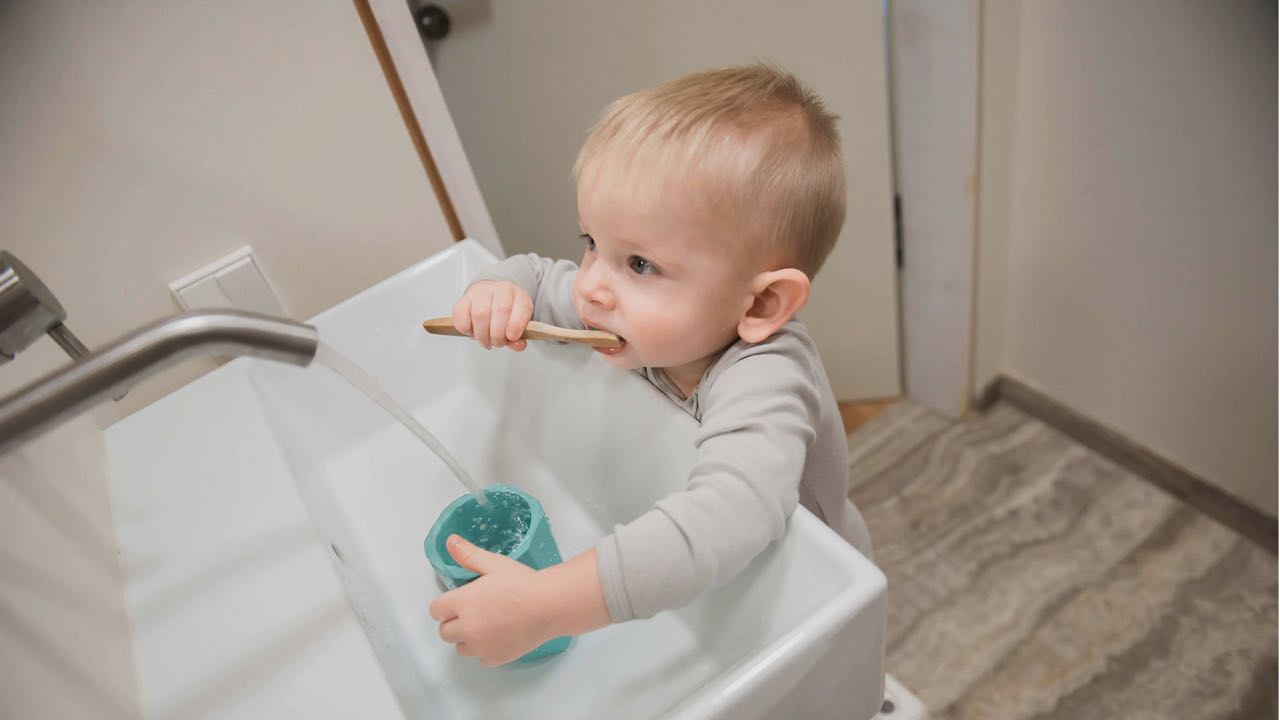 A 2 year old brushing his teeth at the bathroom sink.