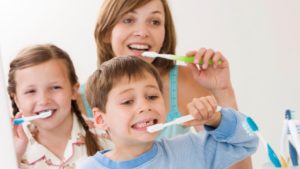 A mother, son and daughter all brushing their teeth together in the bathroom.