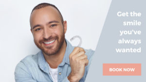 Invisalign aligner being held by a smiling man who is having his crooked teeth aligned